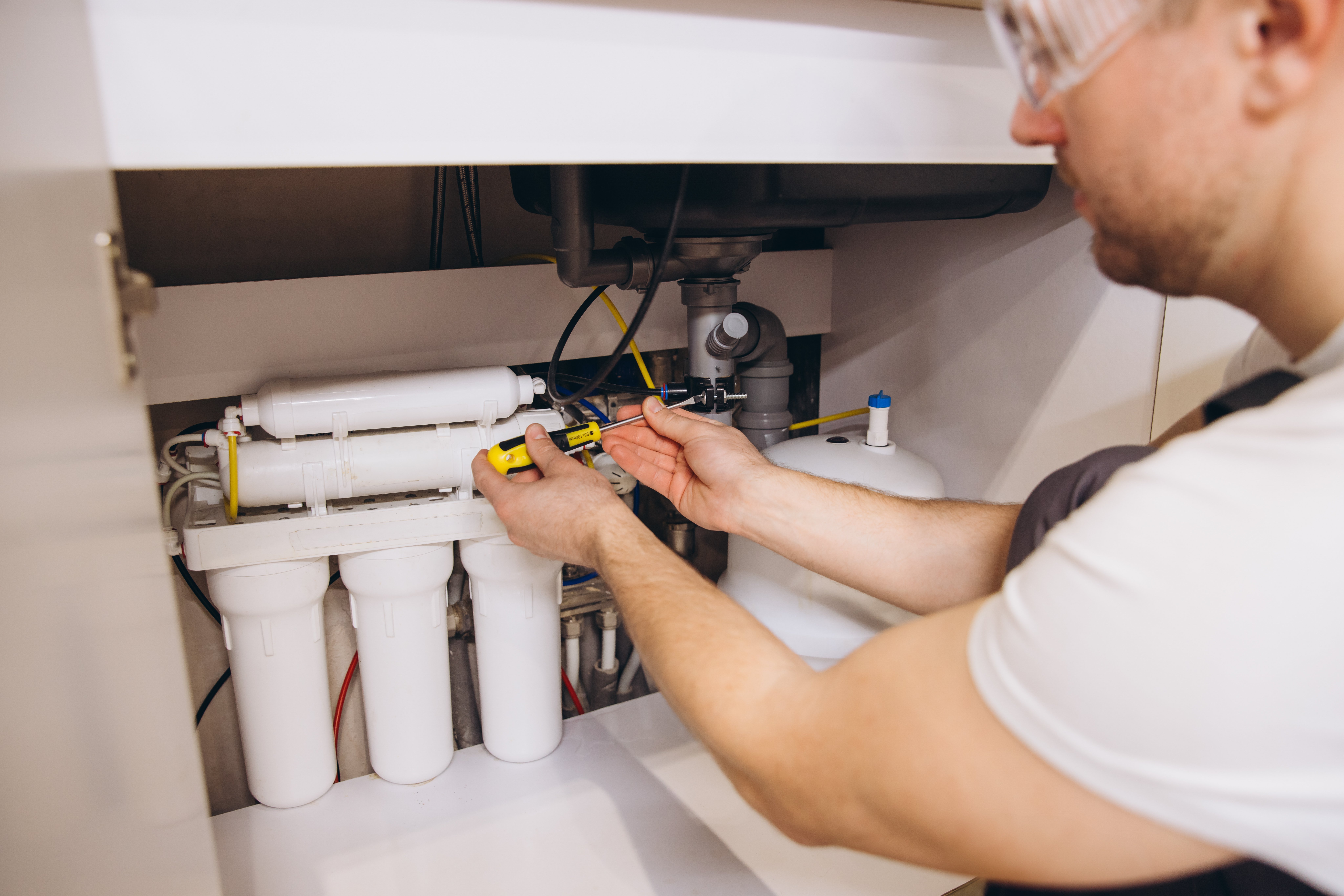 Plumber tightening bolts of water filter cartridges using screwdriver, ensuring clean and safe drinking water in residential kitchen